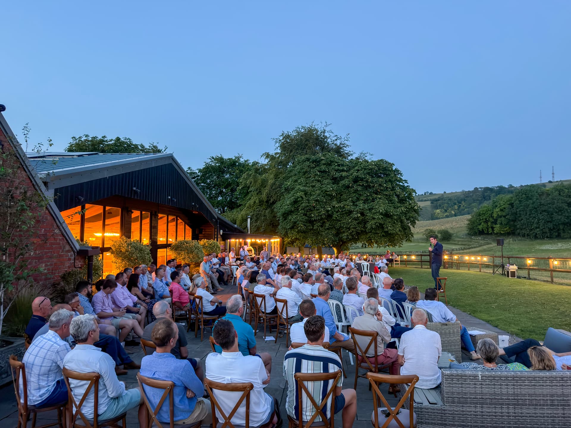 An evening party spilling out of the glowing barn onto the terrace