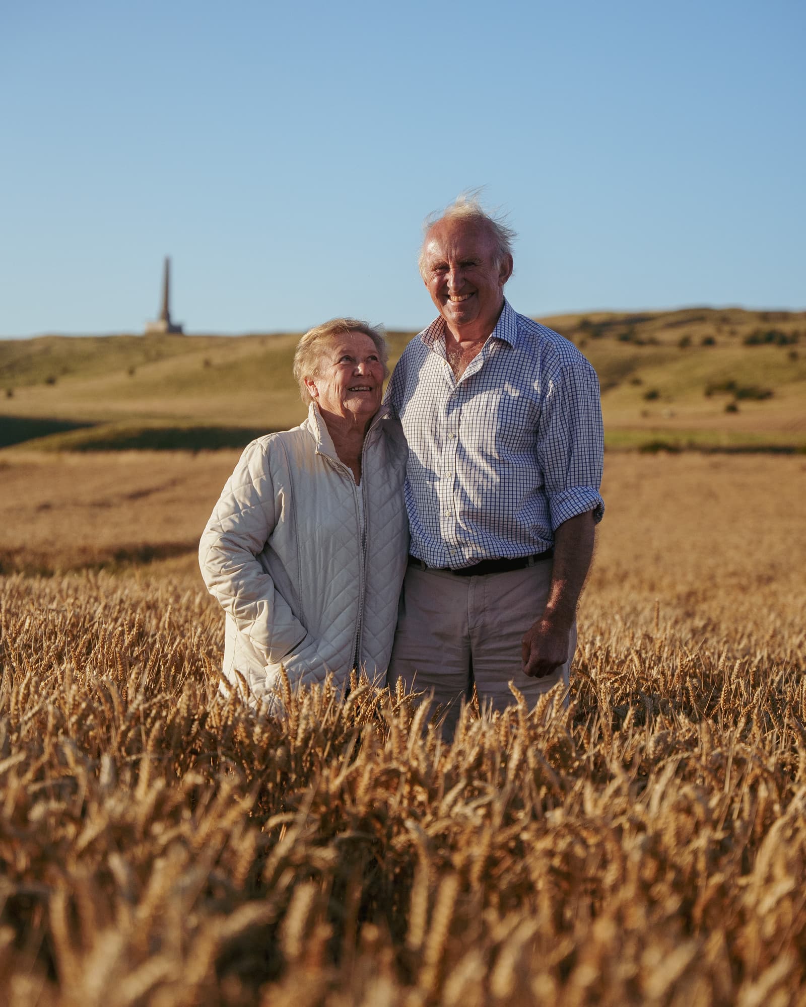 Pat and Sandy standing in the wheat, the Lansdowne Monument on the ridge behind them